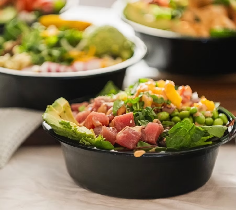 Close-up of a poke bowl with tuna, avocado, edamame, and sauce in a black bowl.