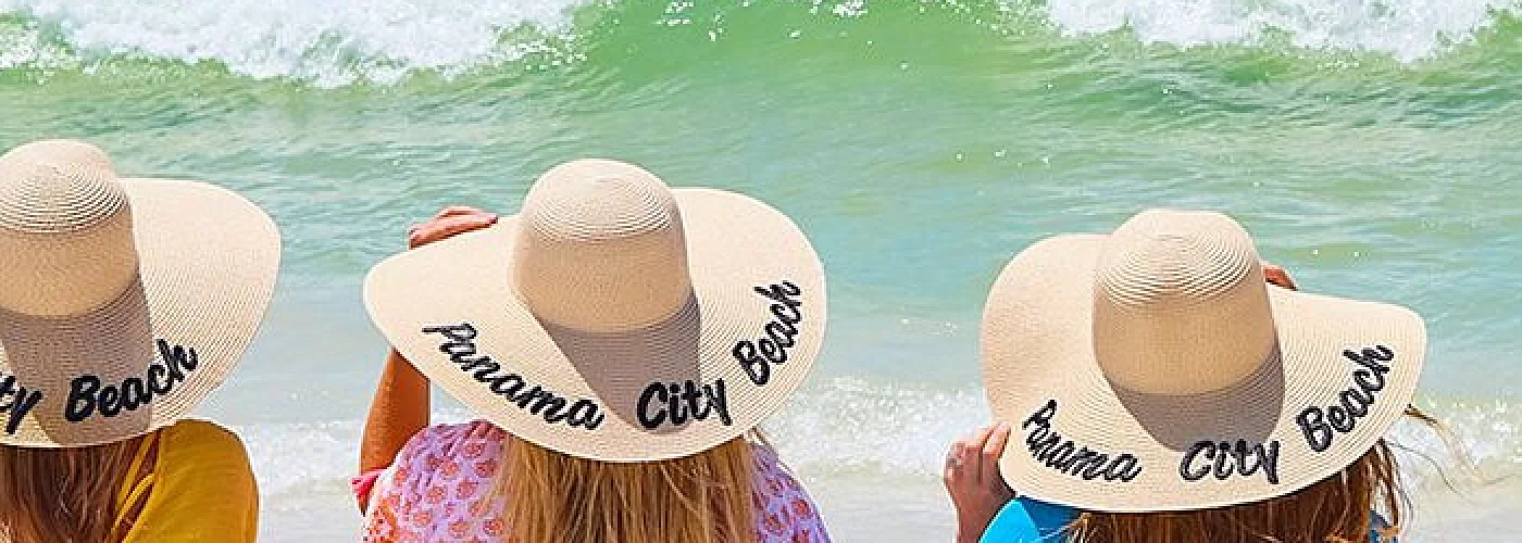 Three women wearing hats on the beach looking at the ocean.