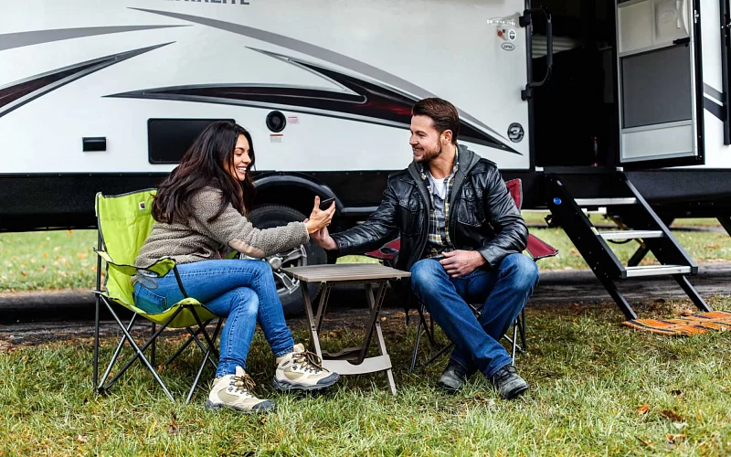A man and a woman are sitting in chairs in front of a rv.