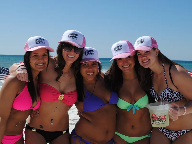 A group of women in bikinis are posing for a picture on the beach