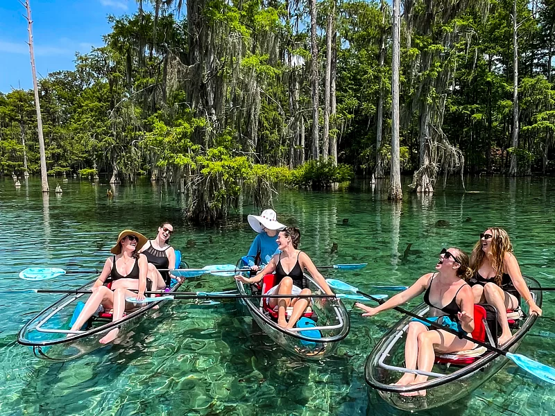 A group of people are sitting in clear kayaks in a lake.