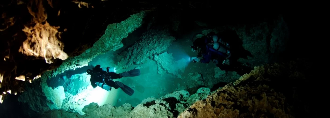 A group of scuba divers are swimming in a cave.