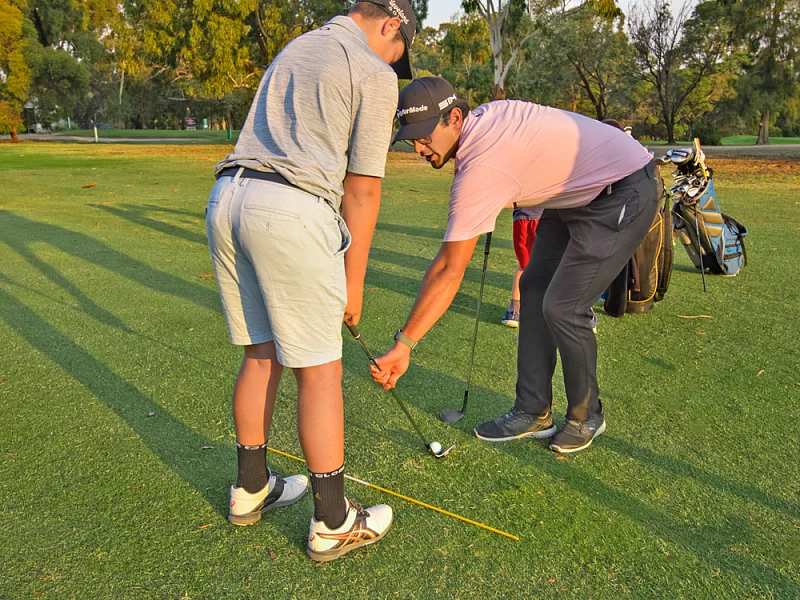 A man is teaching another man how to play golf on a golf course.