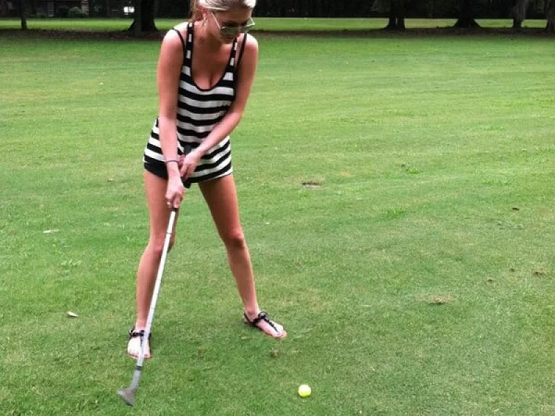 A woman is swinging a golf club at a golf ball
