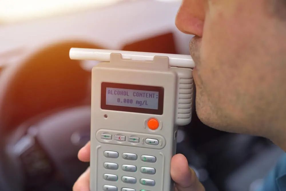 A Man is Drinking From a Breathalyzer in a Car — Fosters Ace Auto Repairs In Aitkenvale, QLD