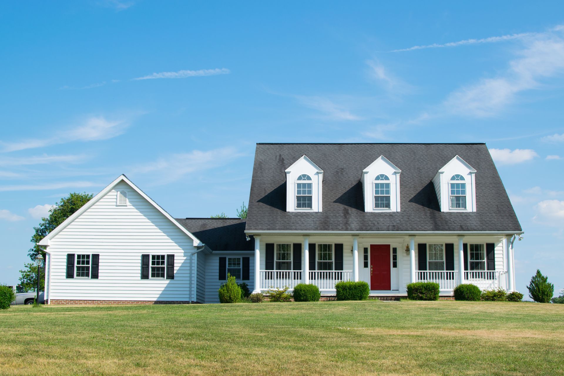 White two-story house with black roof, red door, and green lawn under a blue sky. White two-story house with black roof, red door, and green lawn under a blue sky.