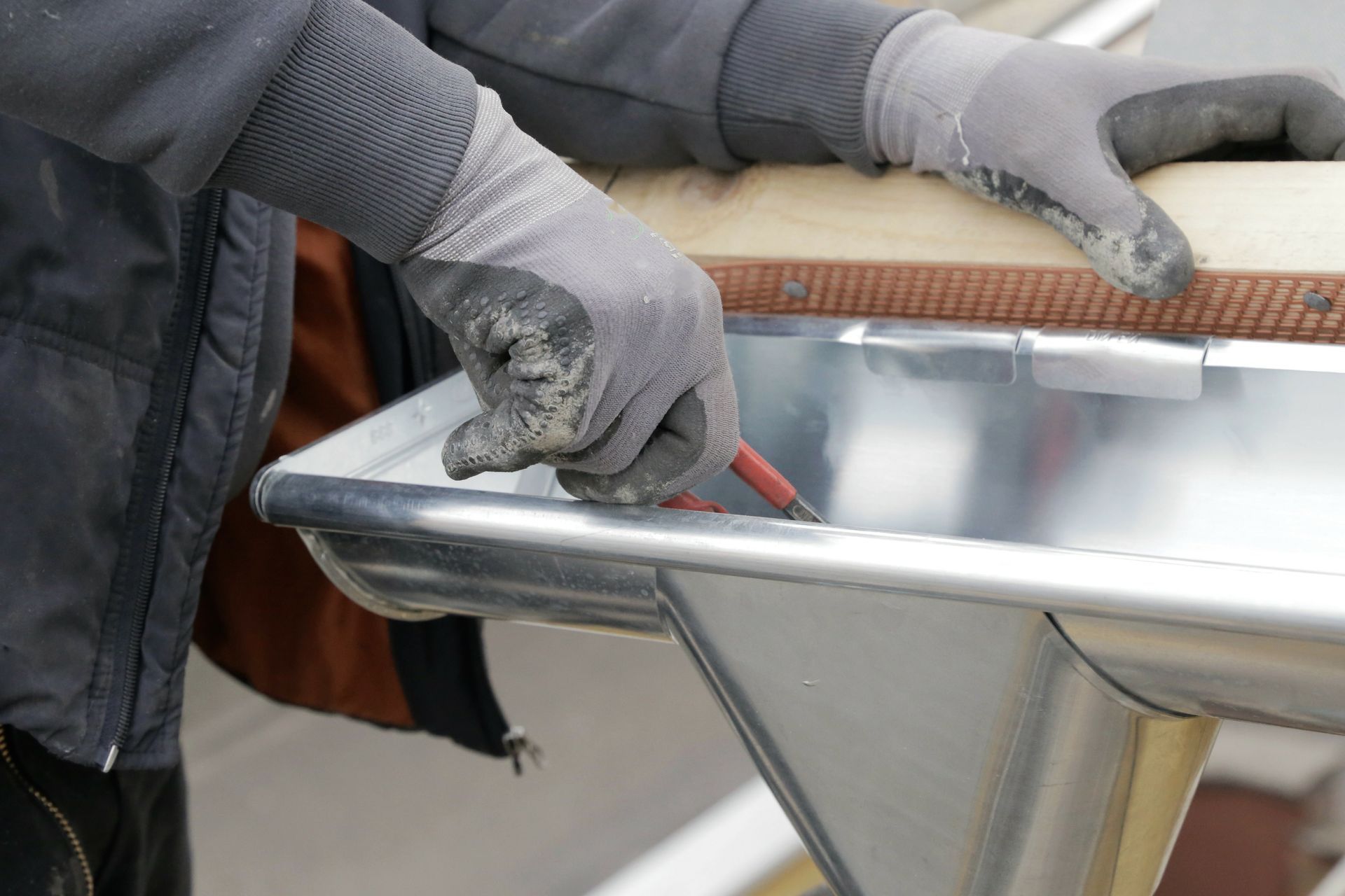 Person marking a metal gutter with a pencil while wearing gray work gloves. Person marking a metal gutter with a pencil while wearing gray work gloves.