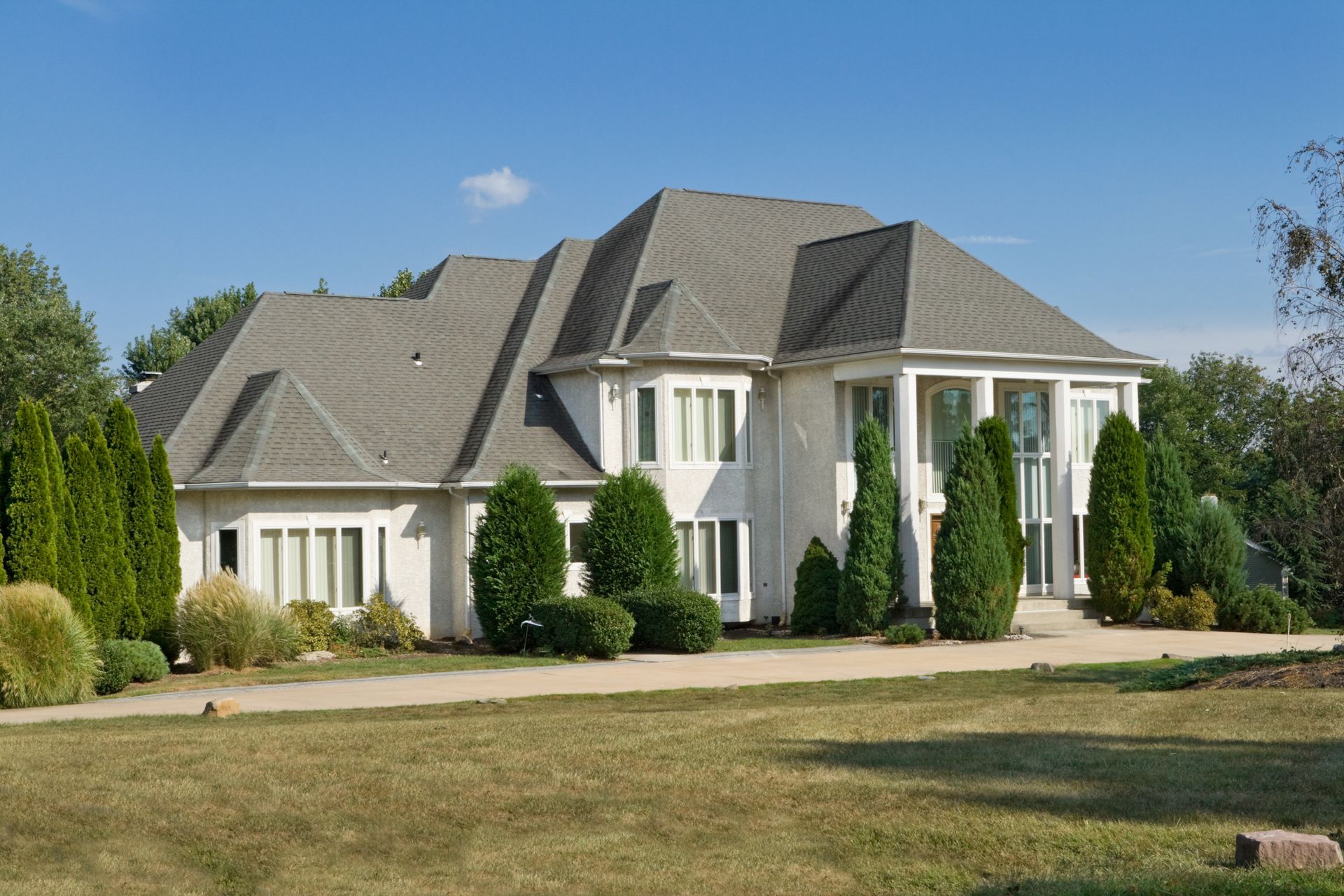 White house with a gray roof, lawn, and trees under a blue sky. White house with a gray roof, lawn, and trees under a blue sky.