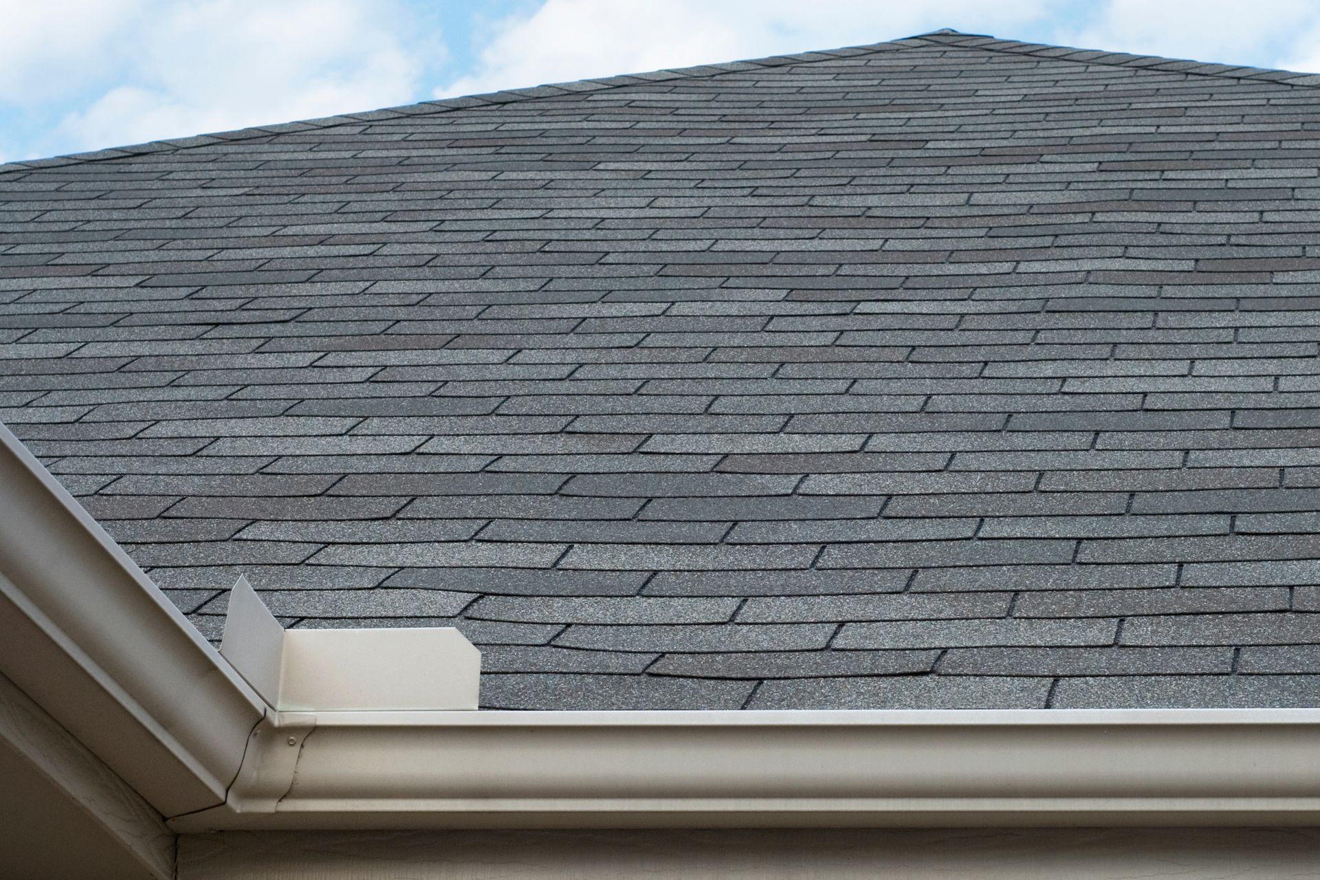 Black roof with matching gutters and downspout against a blue sky. Black roof with matching gutters and downspout against a blue sky.