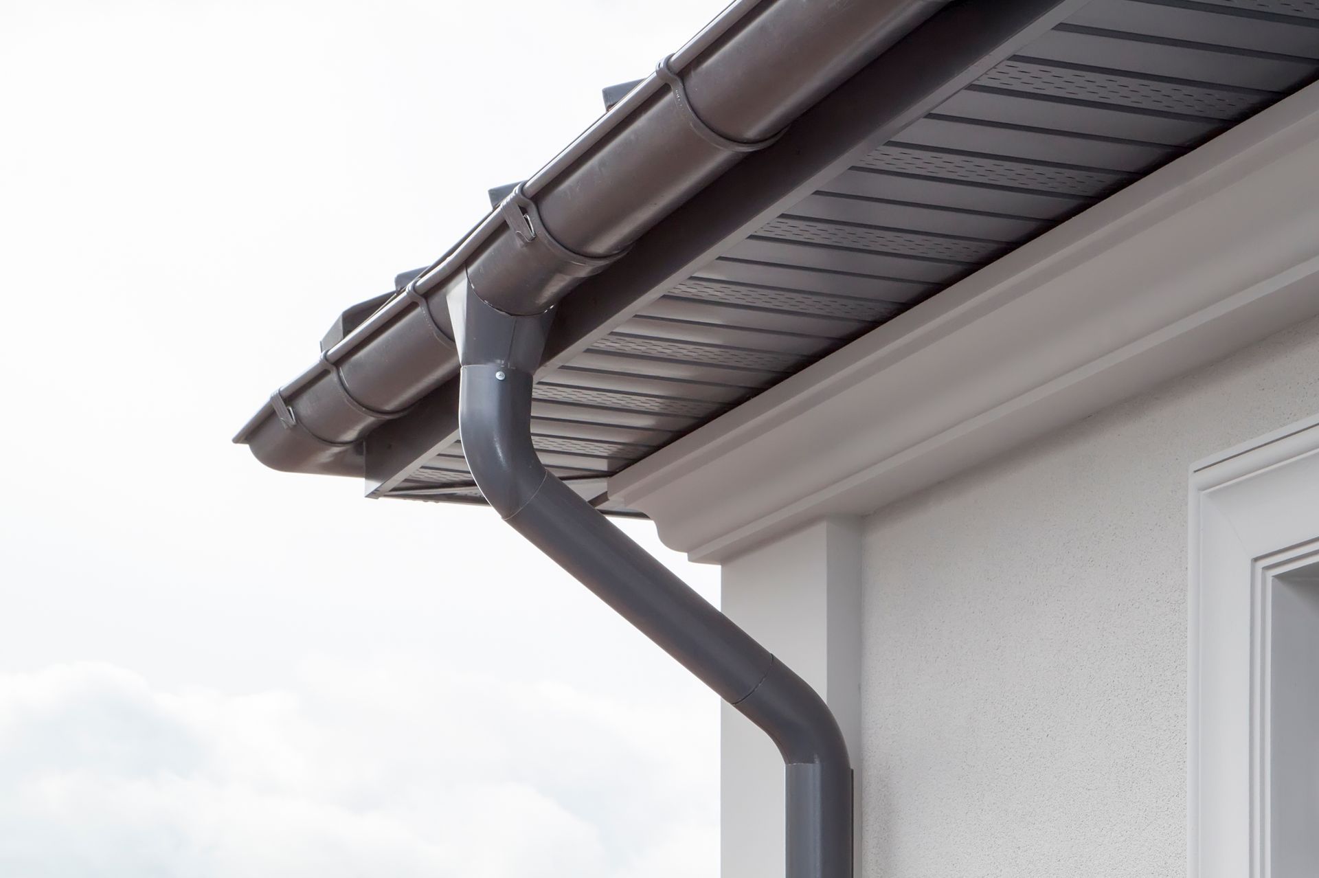 Brown rain gutter and downspout on a house with white trim. Brown rain gutter and downspout on a house with white trim.