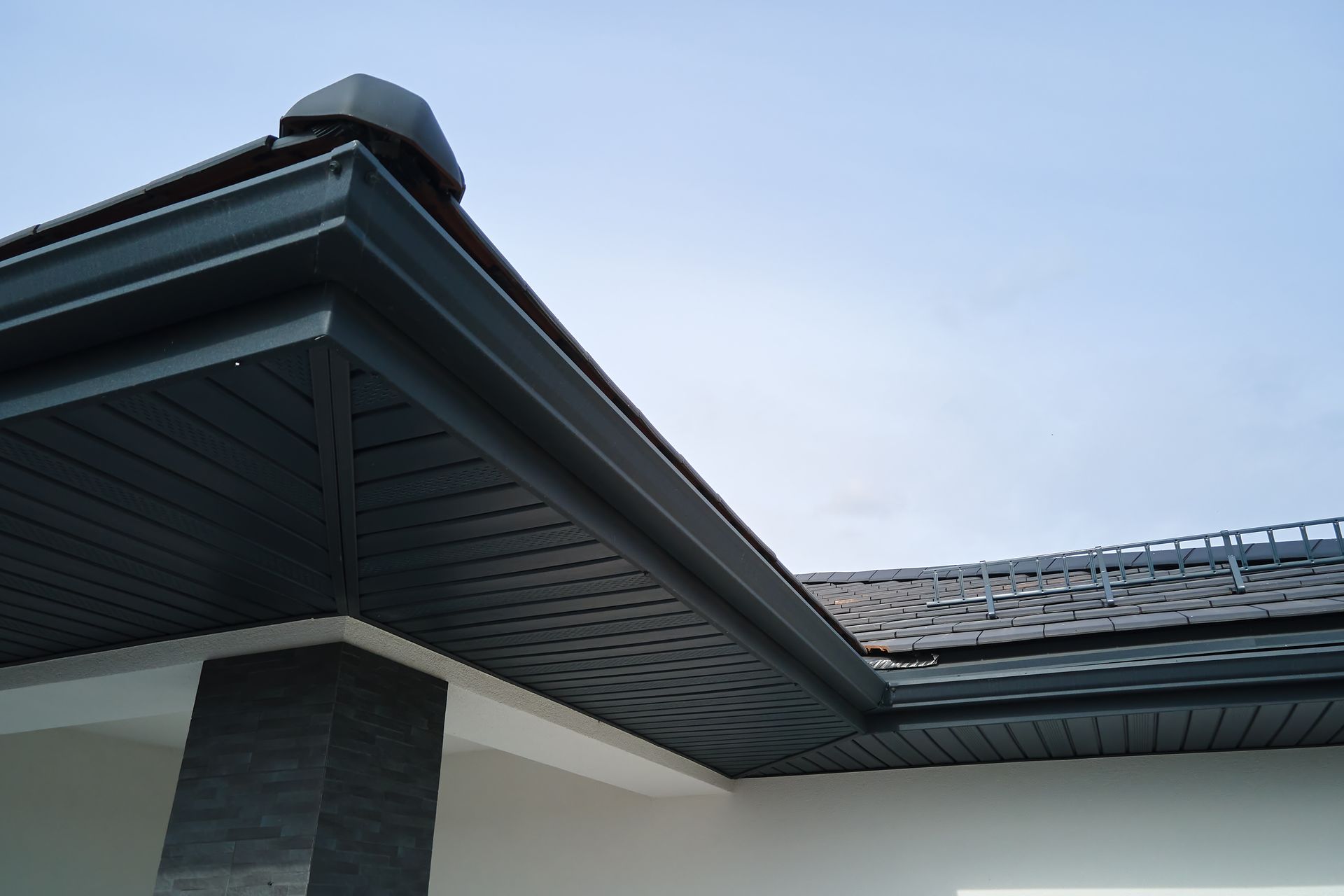 Dark gray roof overhang with gutters against a blue sky.