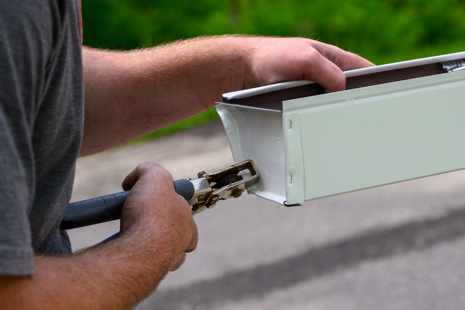 Person using tool to crimp edge of white metal gutter. Person using tool to crimp edge of white metal gutter.