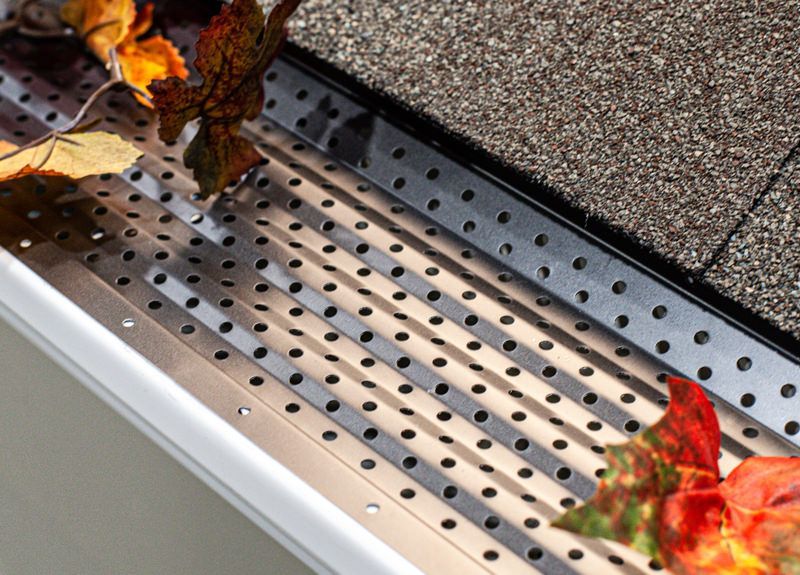 Gutter with black mesh guard installed near roof shingles to prevent debris accumulation. Gutter with black mesh guard installed near roof shingles to prevent debris accumulation.