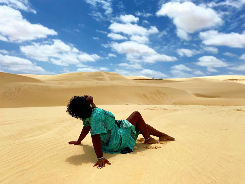 A woman in a green dress is laying on the sand in the desert.