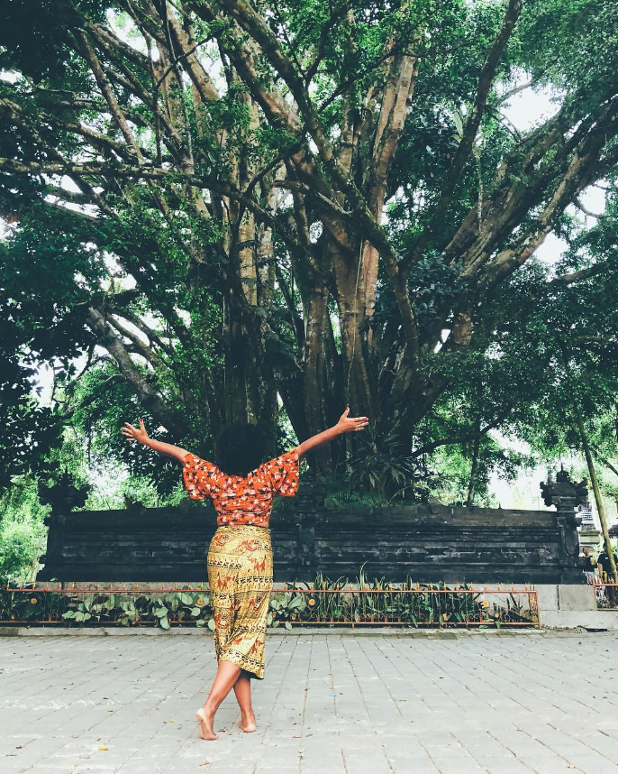 A woman is standing in front of a tree with her arms outstretched