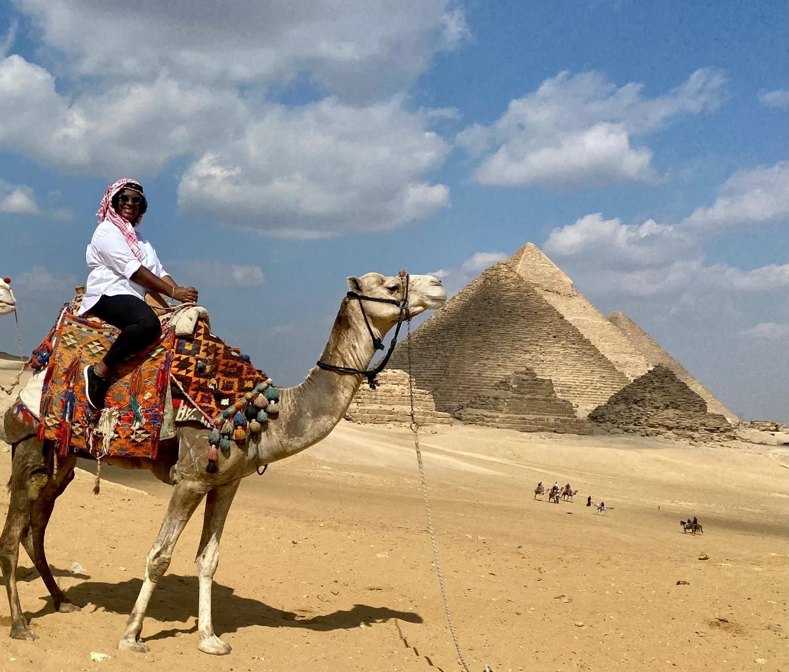 A woman is riding a camel in front of the pyramids