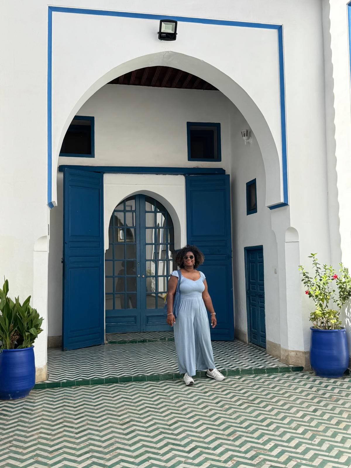 A woman in a blue dress is standing in front of a white building with blue doors.
