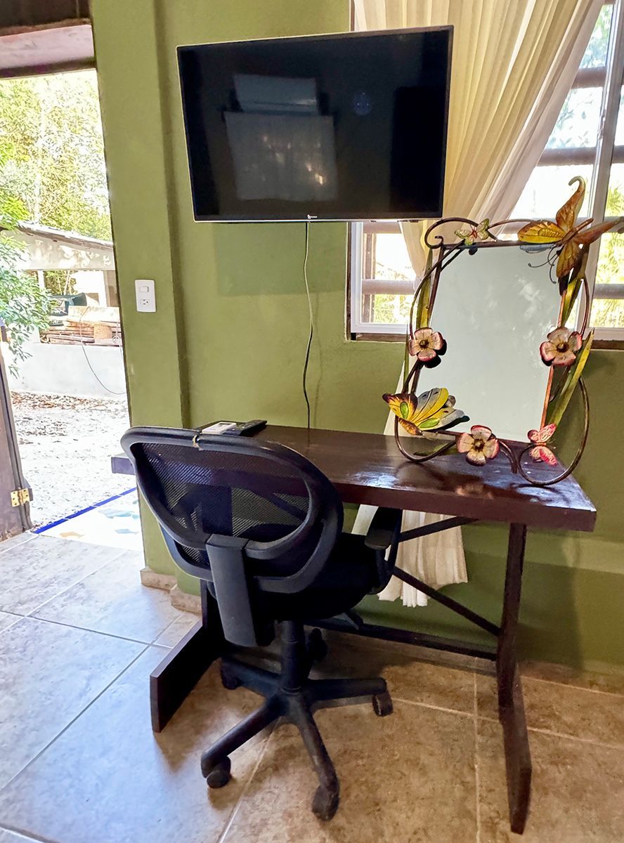 A desk with a chair and a television on the wall above it.