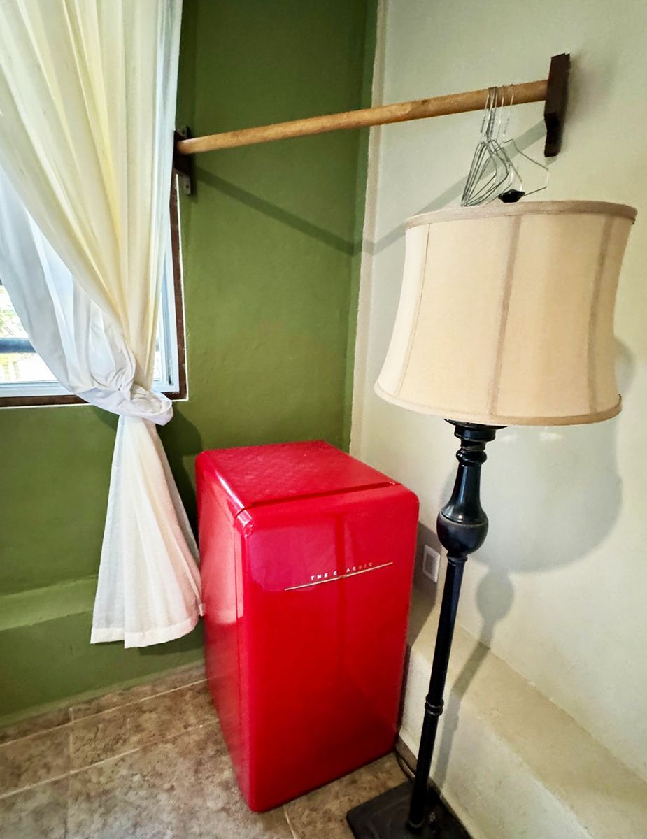 A lamp is sitting next to a red refrigerator in a room.