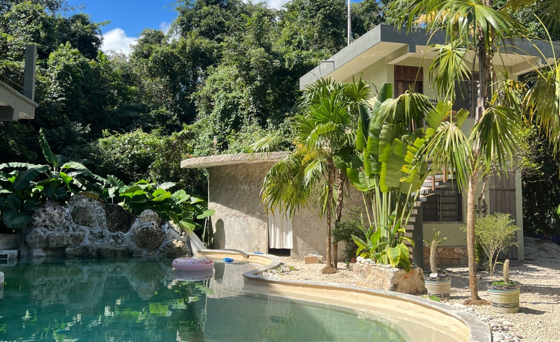 There is a large swimming pool in front of a house surrounded by trees.
