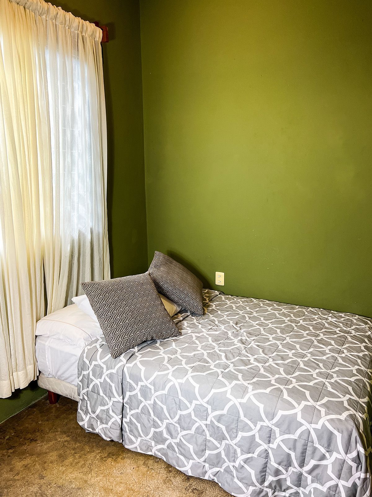 A hotel room with a bed and a window with green walls.