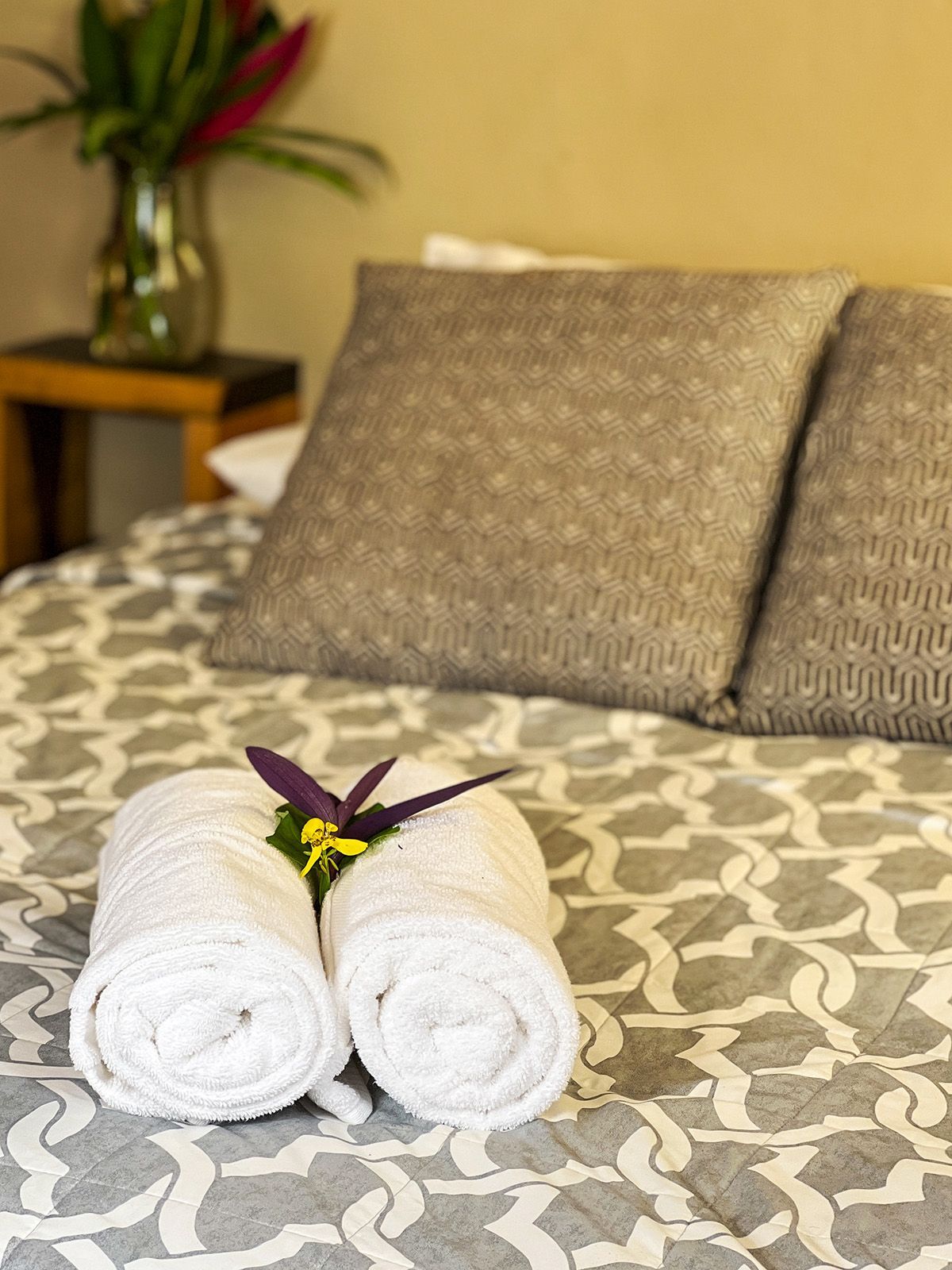 A bed with two rolled towels and a flower on it.