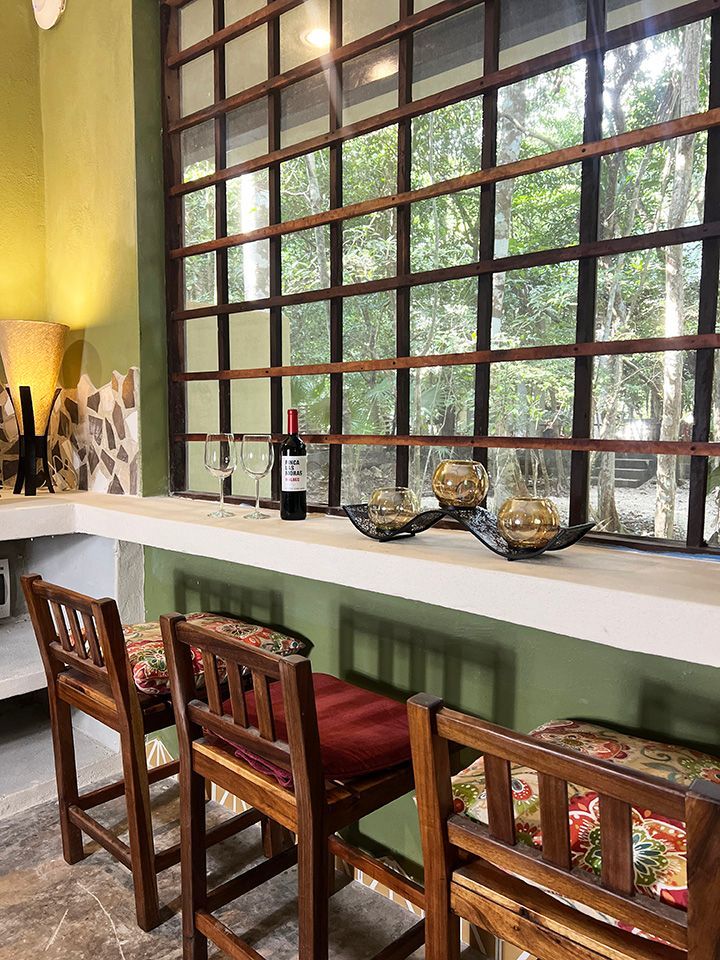 A bar with stools and a bottle of wine on it in front of a window.