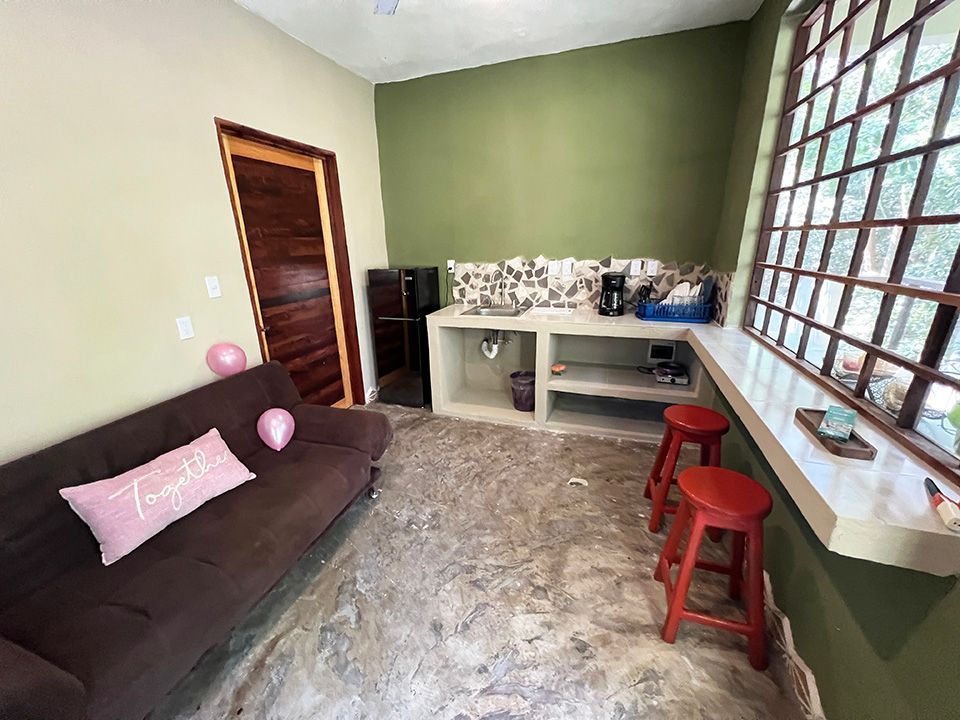 A living room with a couch , stools , and a kitchen.