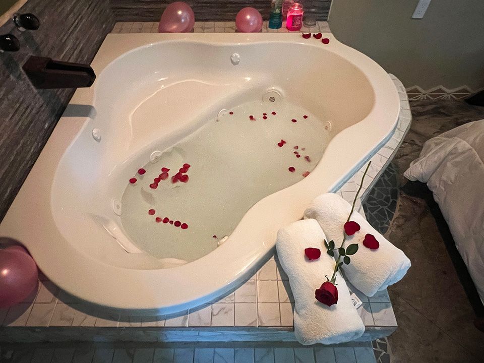 A jacuzzi tub filled with water and rose petals in a hotel suite.
