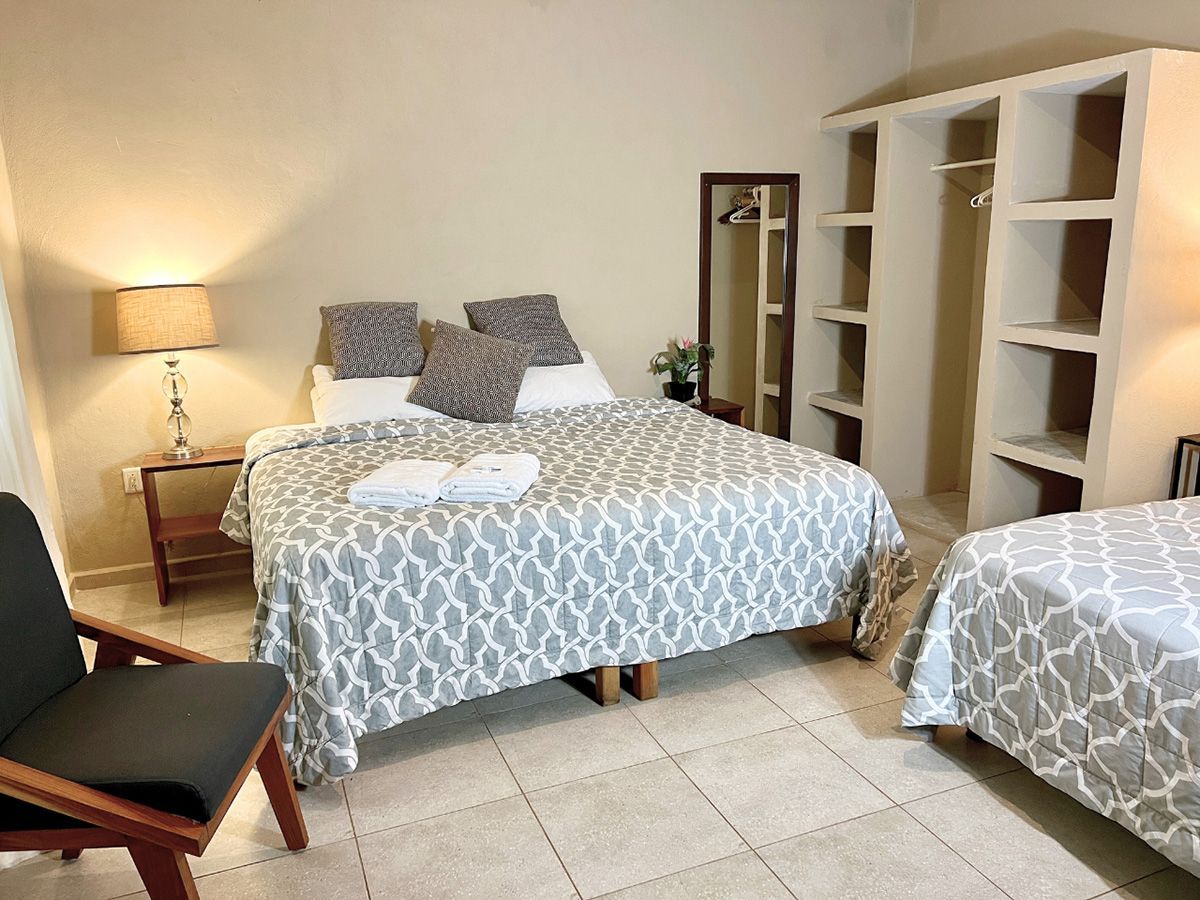 A hotel room with two beds , a chair , a lamp and a mirror.
