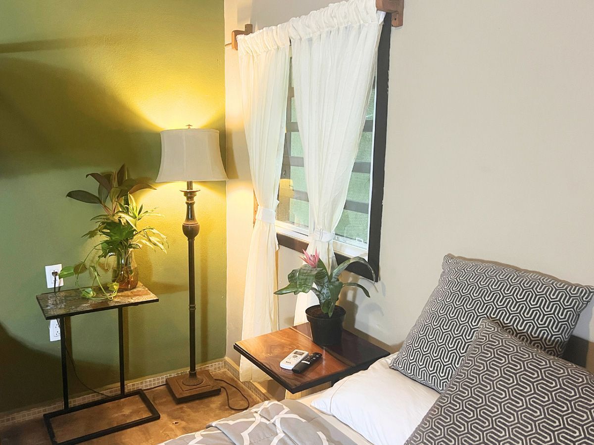 A hotel room with a bed , nightstand , lamp and window.