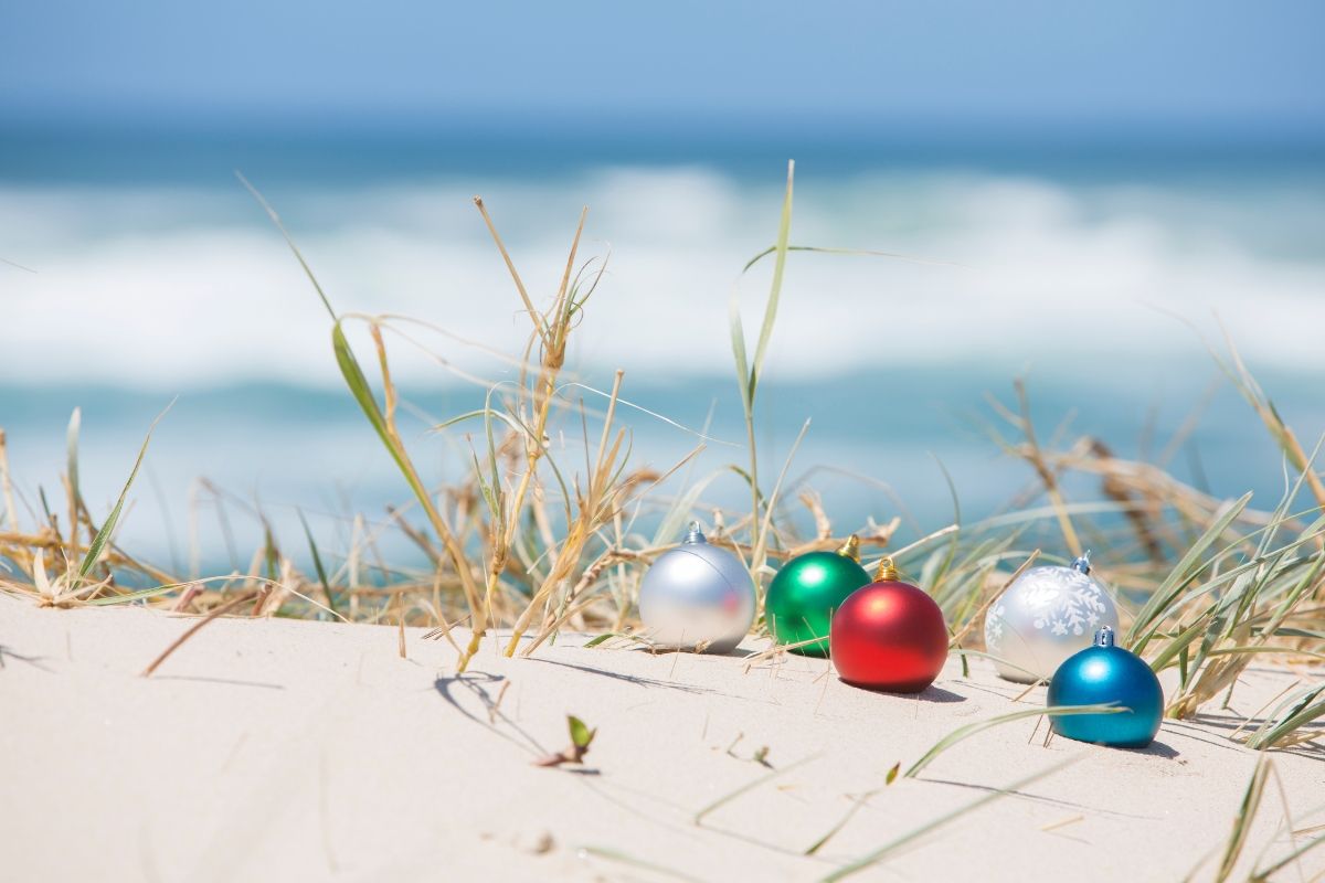 Colorful Christmas ornaments nestled in the sandy dunes of Carolina Beach, with ocean waves and sea grass in the background, capturing the festive coastal charm of the holiday season.