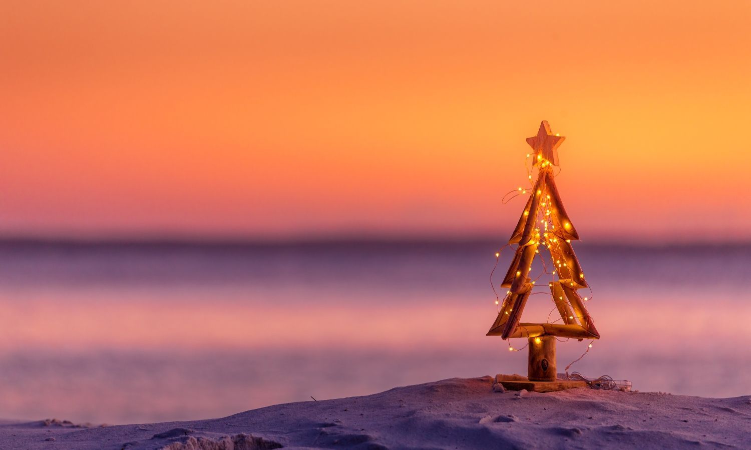 A small wooden Christmas tree decorated with twinkling lights on the sandy shores of Carolina Beach.