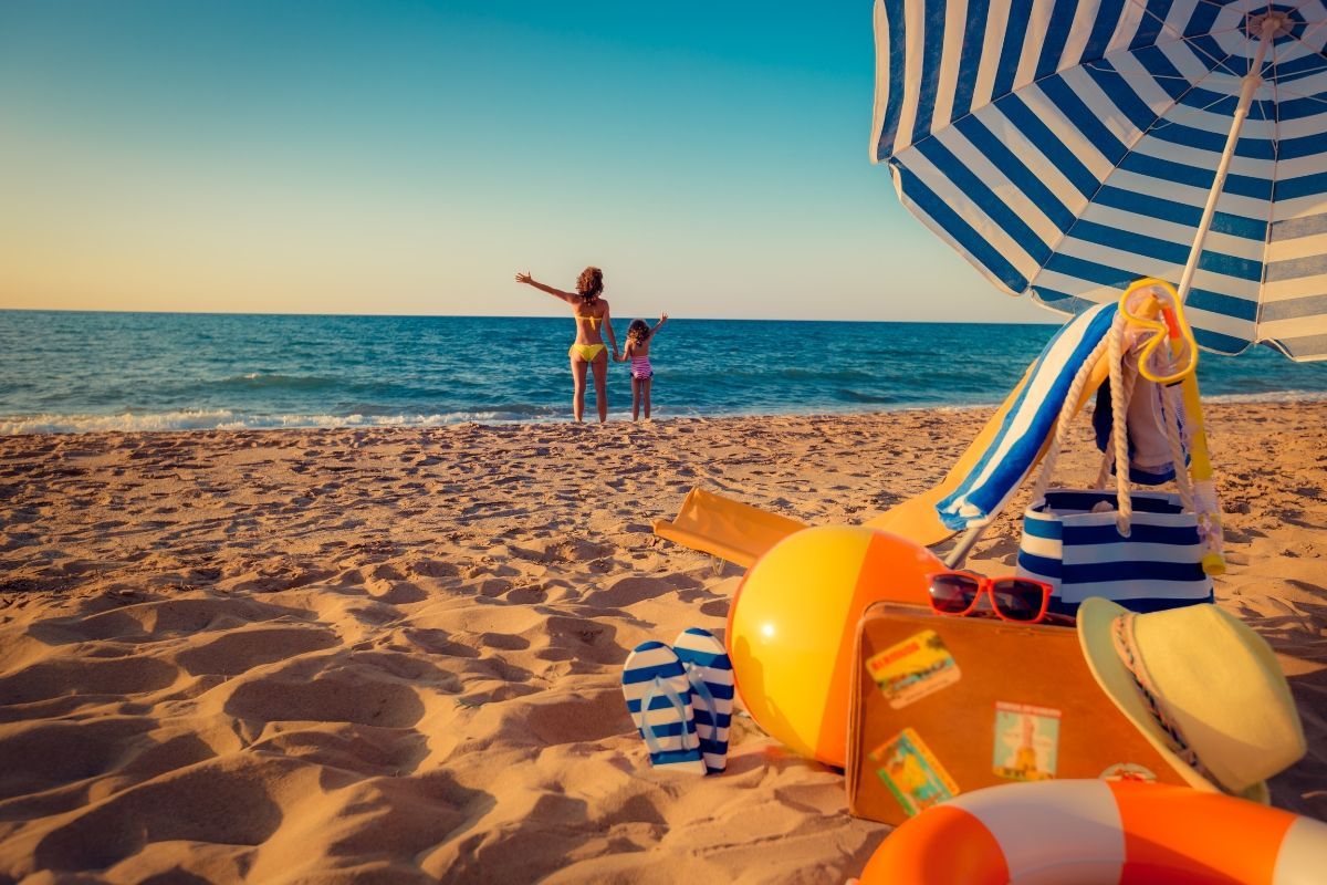 A vibrant beach scene near Carolina Beach Inn with a striped umbrella, colorful beach toys, and a suitcase in the sand.