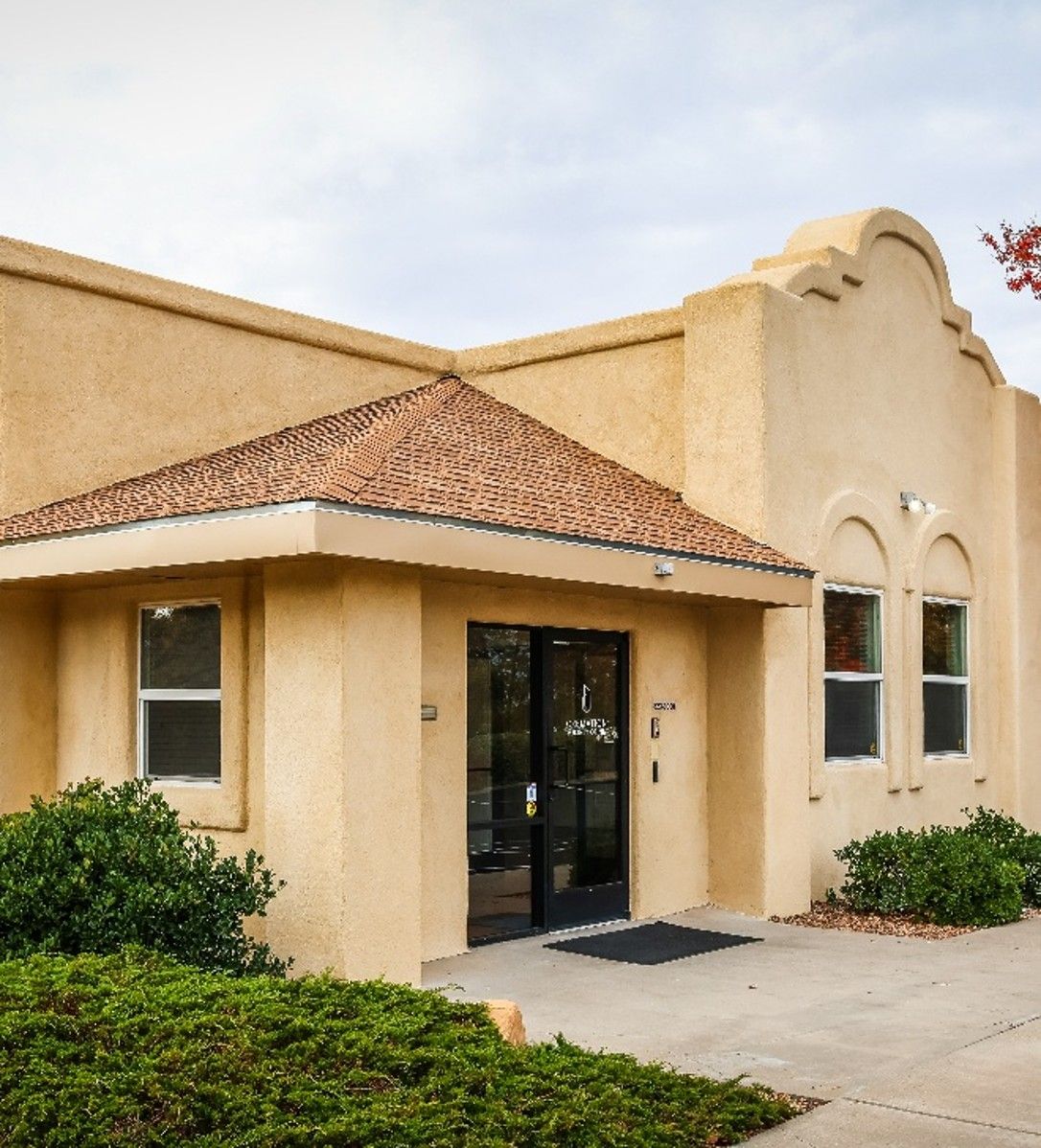Adobe-style building entrance with tan stucco walls, red-tile roof, and black double doors