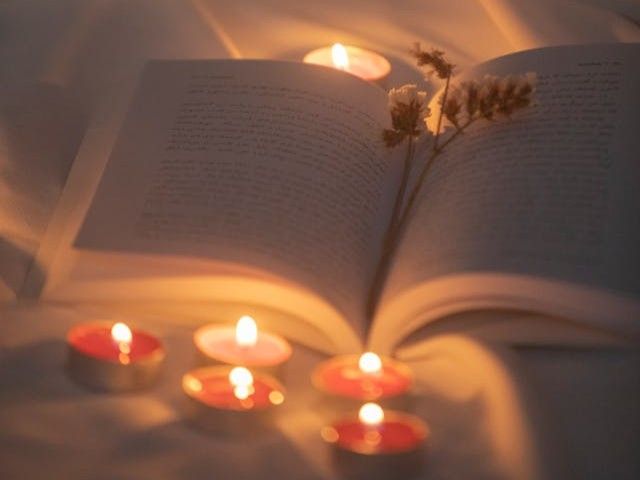 A glowing tealight rests on an open book beside flowers, creating a quiet tribute in Rio Rancho, NM