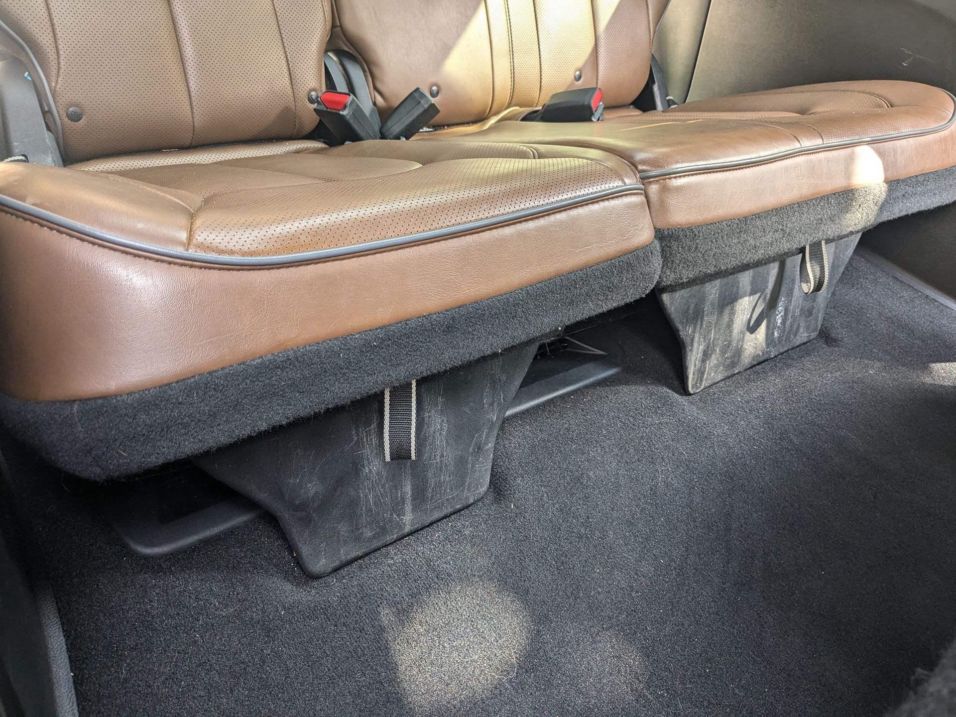 Interior of a vehicle showing the tan, perforated leather rear bench seat with black carpet flooring.