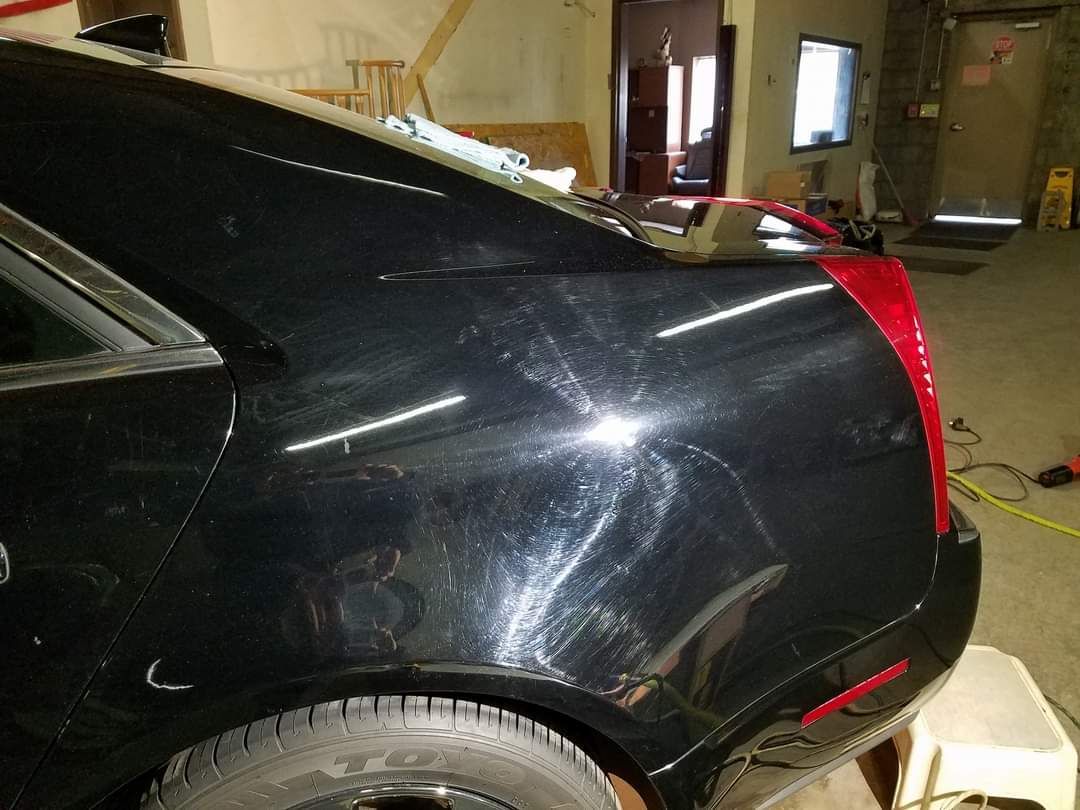 A black car with a red tail light is parked in a garage.