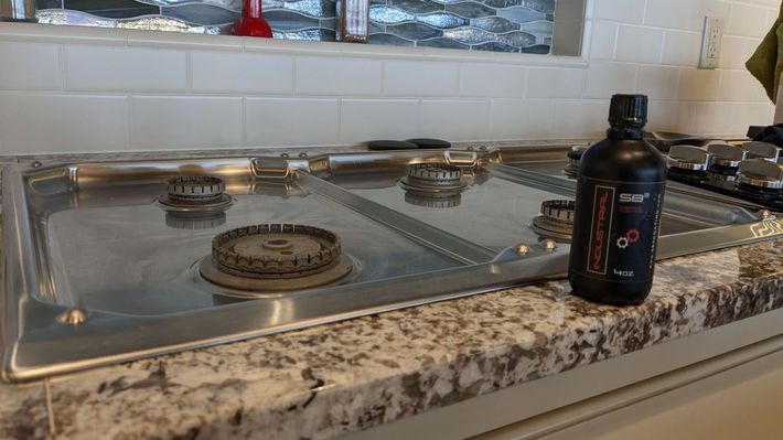 A bottle of oil is sitting on a kitchen counter next to a gas stove.