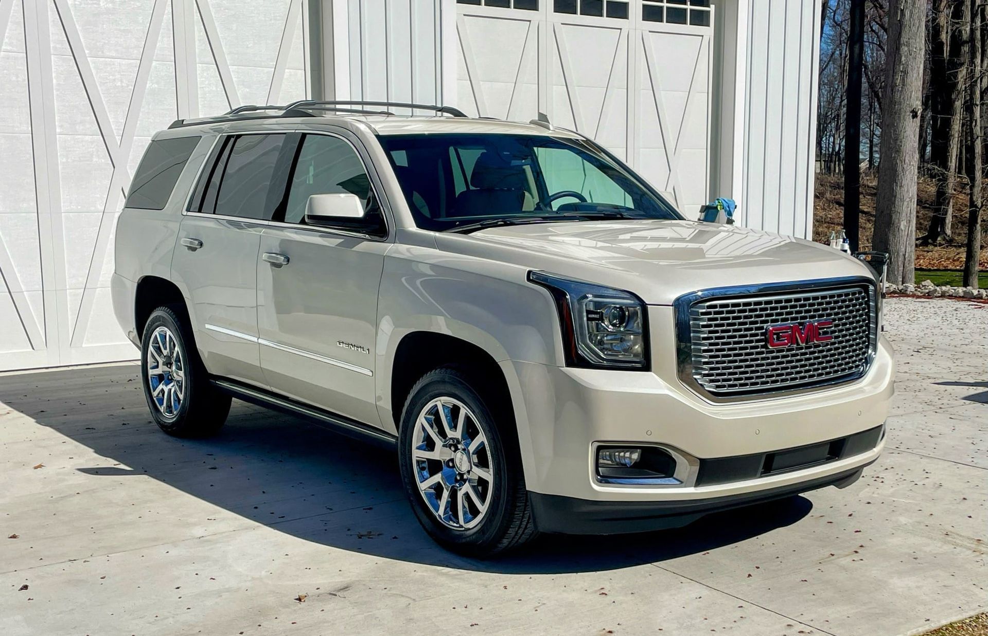 A beige GMC Yukon SUV parked on a concrete driveway in front of a white barn.