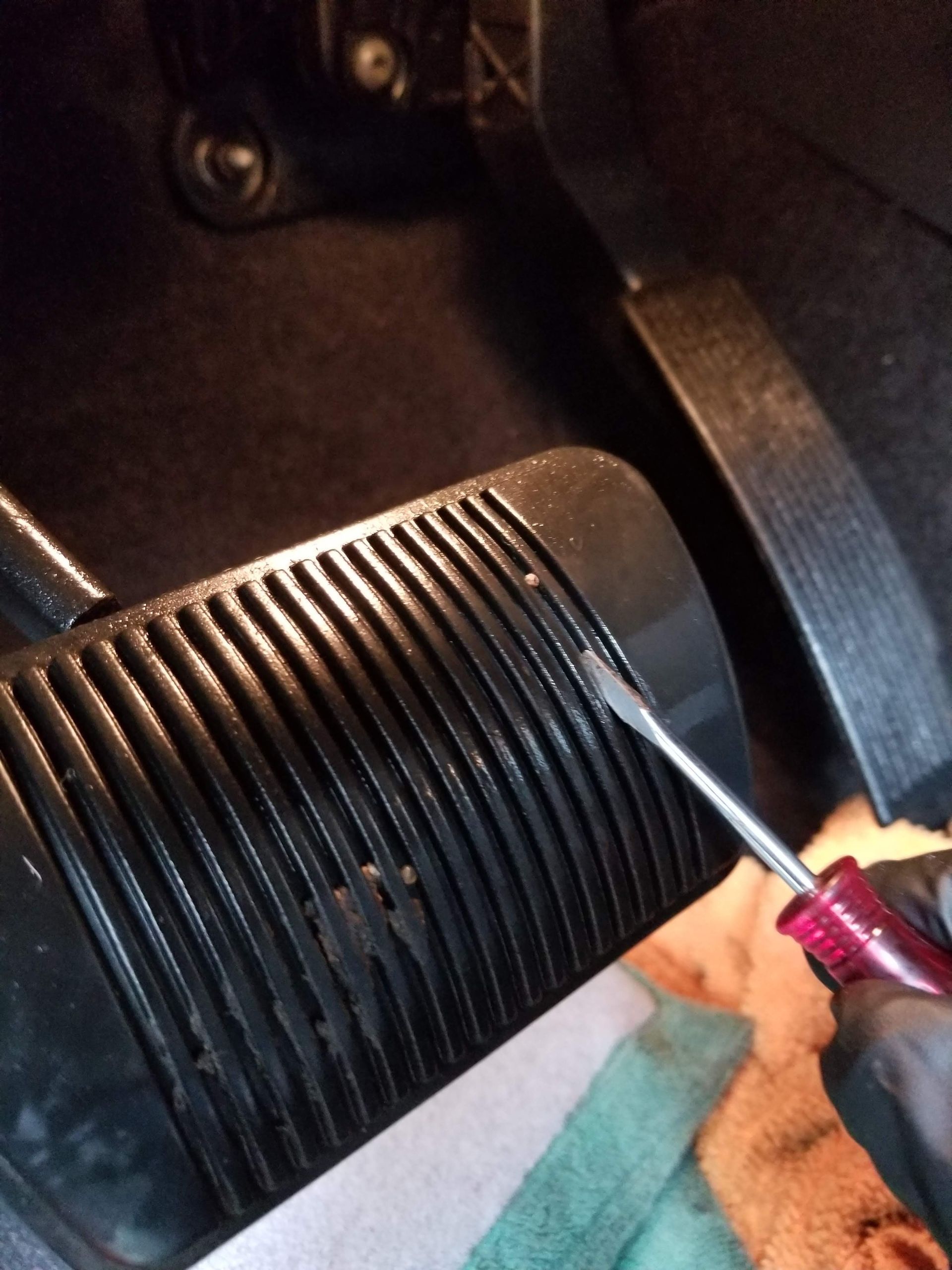A person is using a screwdriver to remove a brake pedal