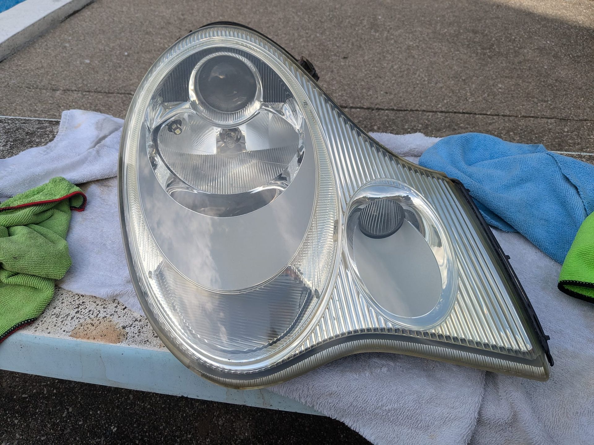 A cleaned, clear automotive headlight assembly resting on white towels outdoors.