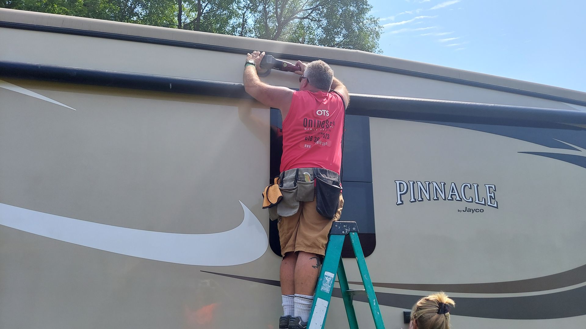 A man is standing on a ladder working on the side of a rv.