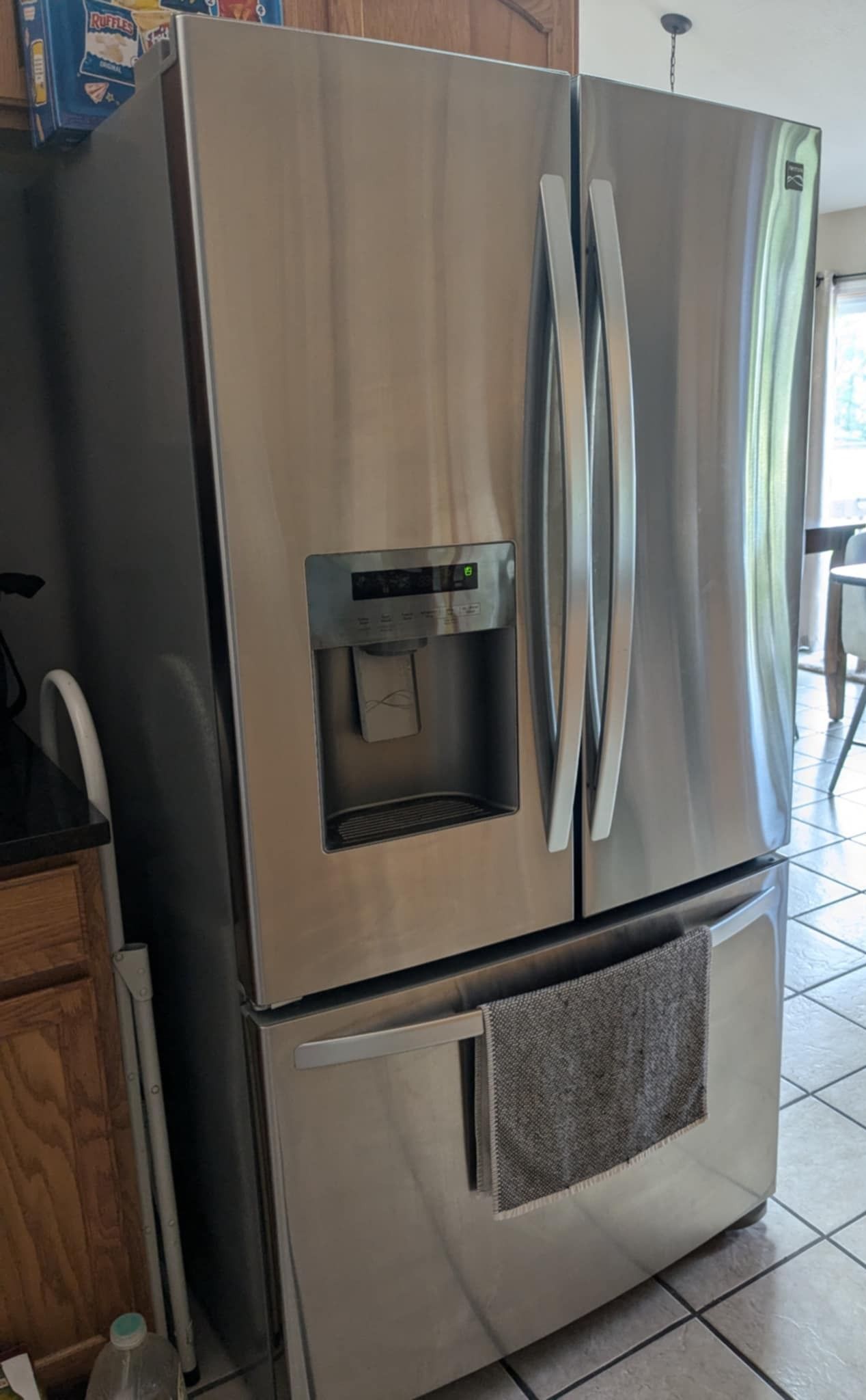 Stainless steel French door refrigerator with an external water and ice dispenser, located in a residential kitchen.