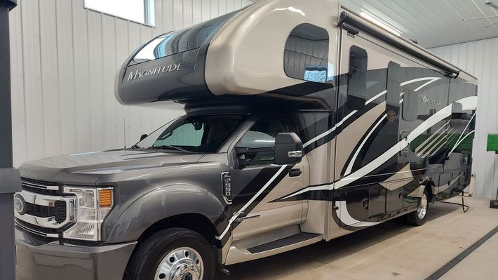 A man is standing on a ladder cleaning the windshield of a rv.
