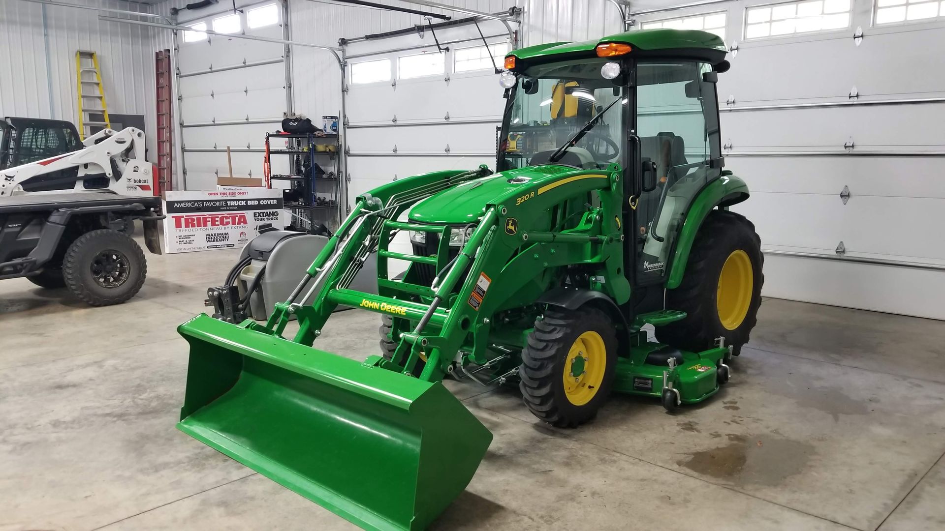 A green john deere tractor is parked in a garage.