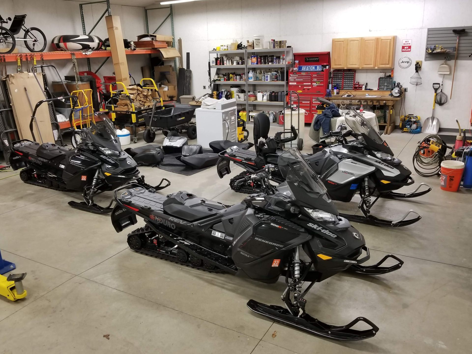 A row of snowmobiles are parked in a garage.