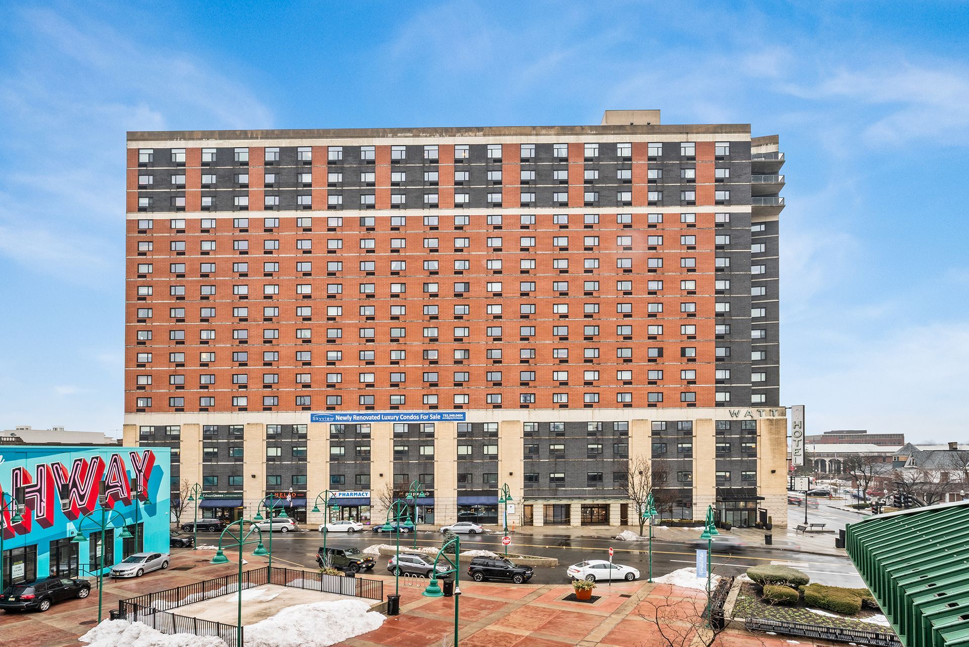 An aerial view of a multi-story red brick apartment complex under construction, surrounded by parking lots and city streets.