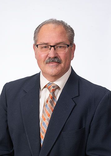 Studio portrait of a man in a navy suit, white shirt, and orange striped tie against a plain white background