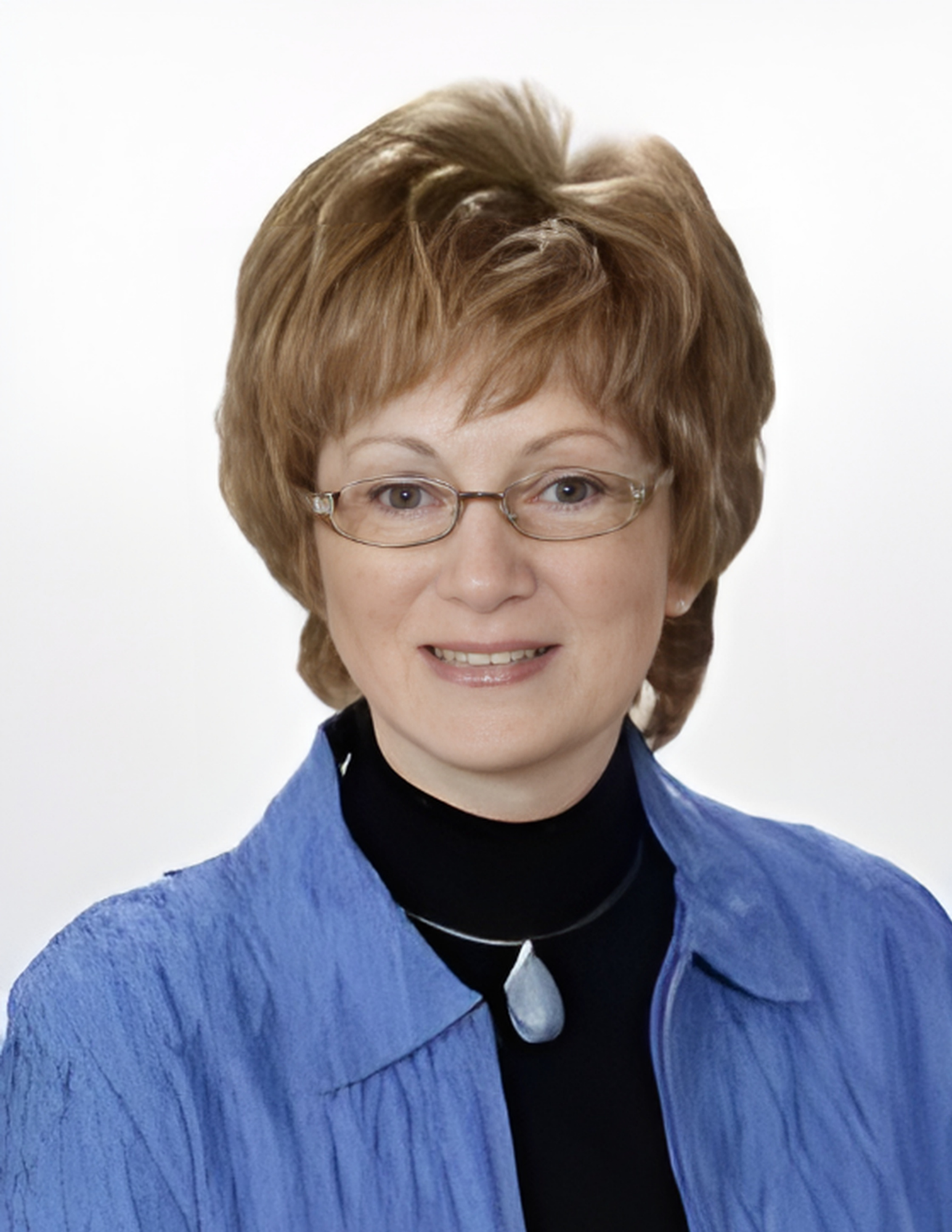 Portrait of a smiling woman wearing glasses, a blue shirt, and a black turtleneck with a pendant necklace